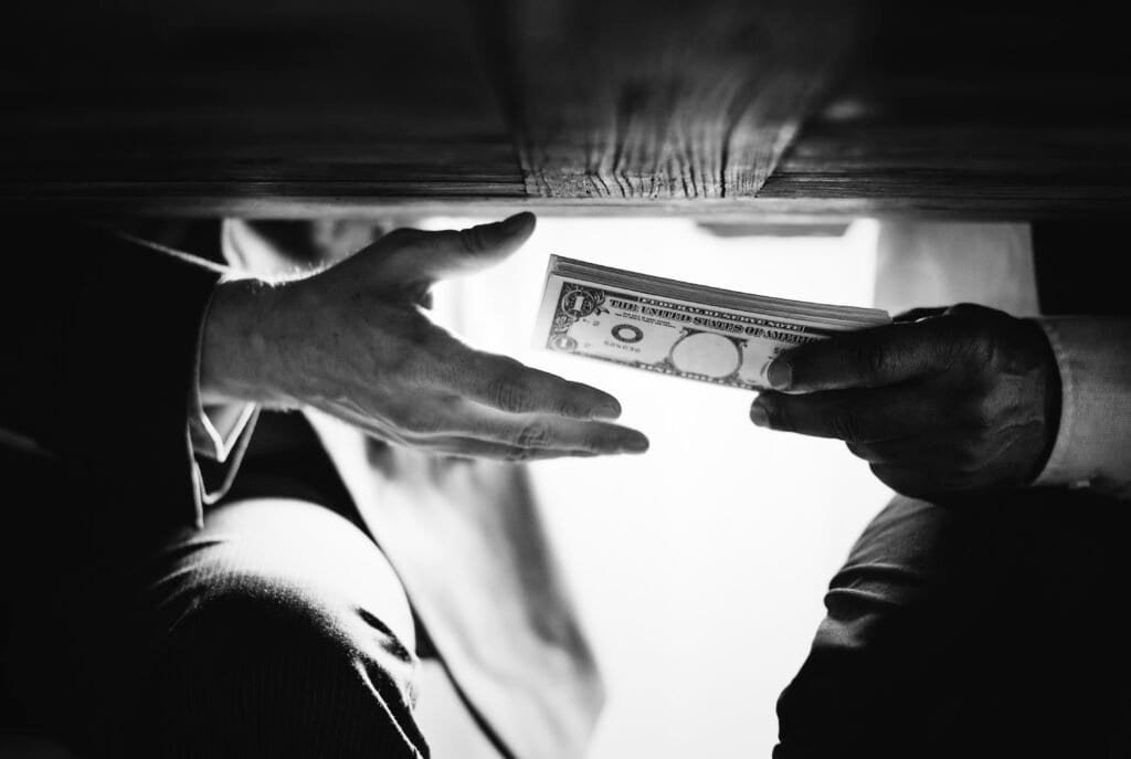 Why Does Human Trafficking Happen? Exploring The Root Causes In Iowa 2 - Hands Passing Money Table Corruption Bribery hands passing money table corruption bribery 2025 Jeremiah Darwin Inc